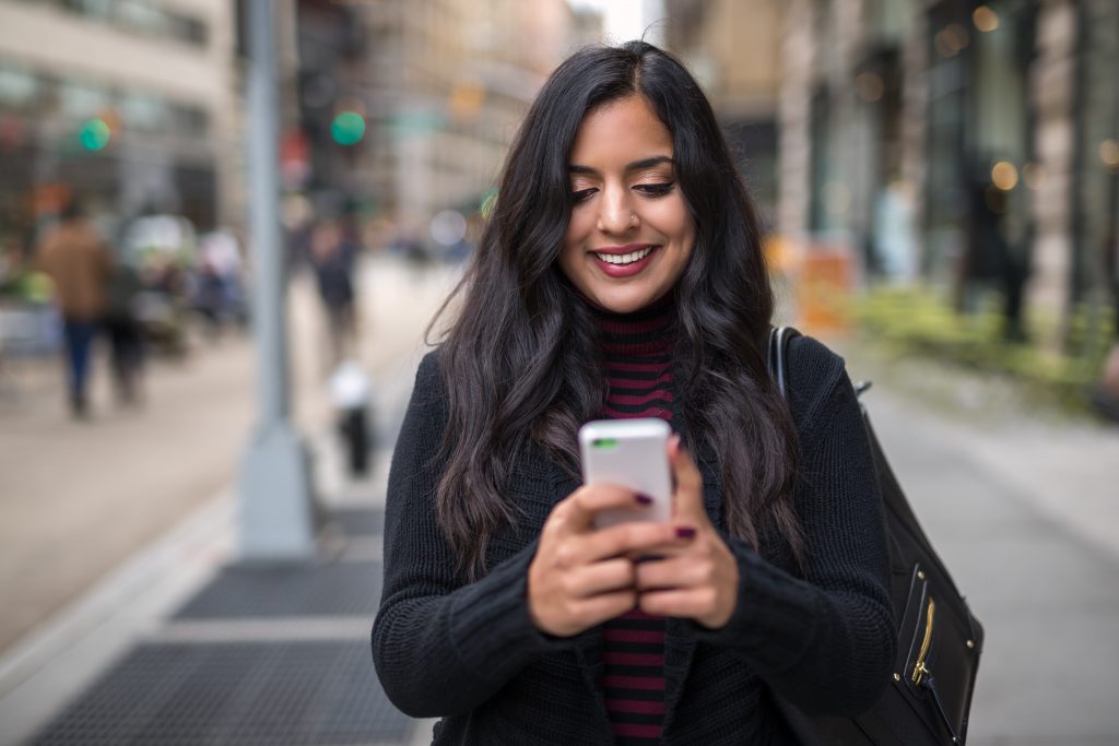 woman smiling while using smartphone in public