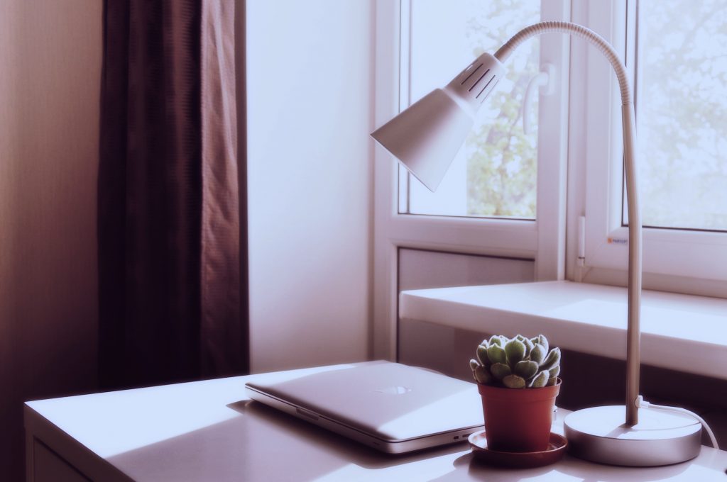 Desk positioned in front of the window with a laptop and lamp on the desk. 
